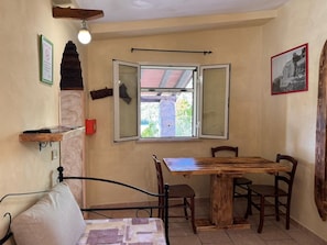 Ein Zimmer mit einem Bett, einem Tisch, Stühlen, einem Fenster mit geöffnetem Klappladen und einem Wandregal.
