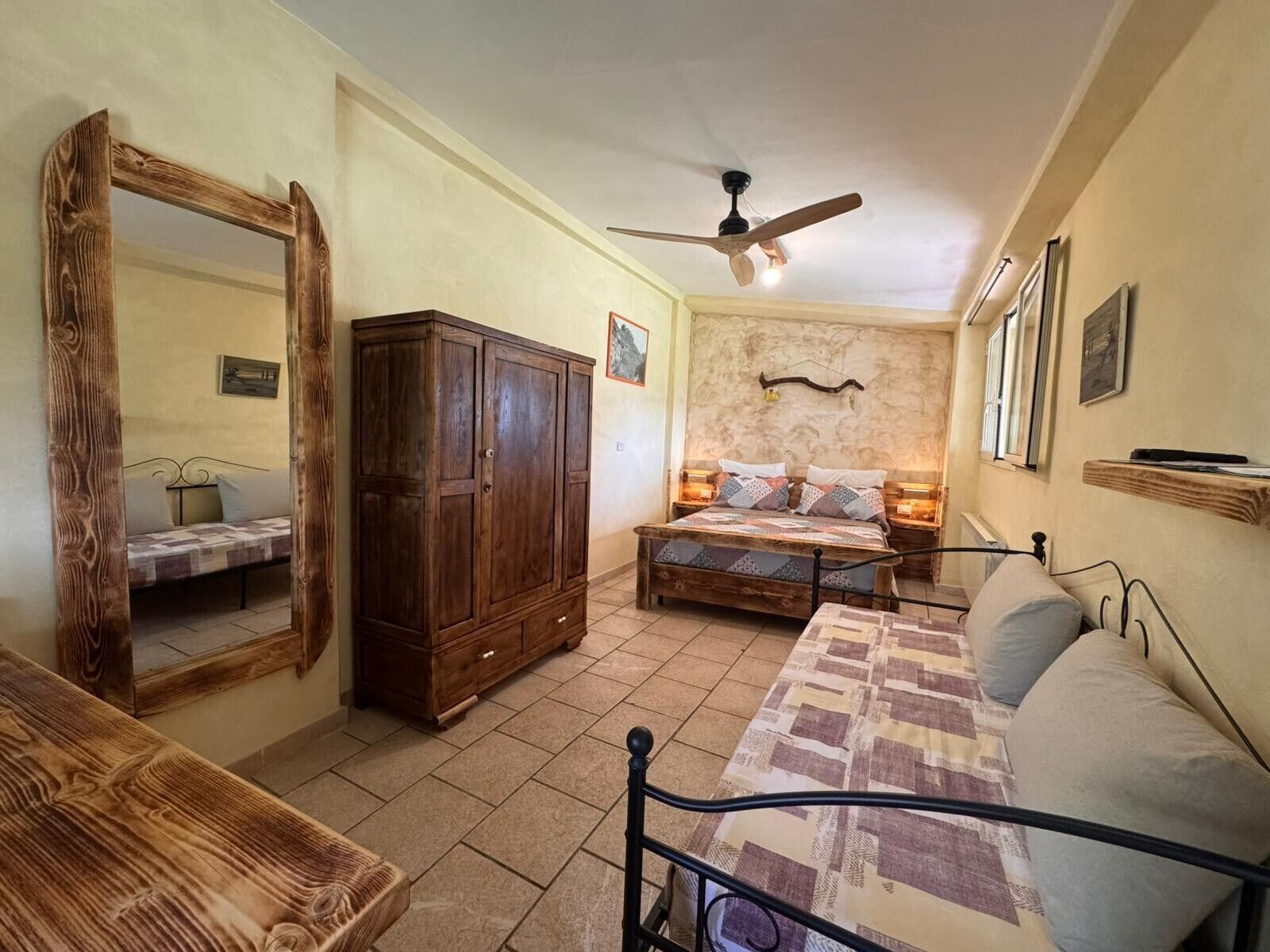 Quarto com cama, guarda-roupa, espelho, ventoinha no teto e janela.