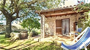 Un edificio de piedra con una pérgola de madera, una silla de lounge y una mesa de piedra.