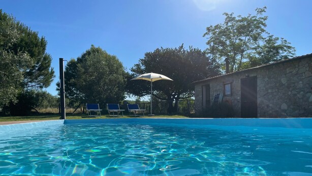 Piscina limpia con agua azul, rodeada de árboles y un edificio de piedra.