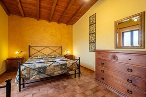 A bedroom with a wooden ceiling, a bed with a metal frame, a wooden dresser, and a wall-mounted mirror.