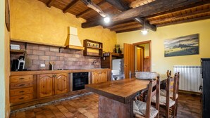 A rustic kitchen with wooden cabinets, a brick wall, and a wooden island with chairs. - Farmhouse "Sasso Bianco" with Shared Pool, Private Terrace & Wi-Fi (Pitigliano)