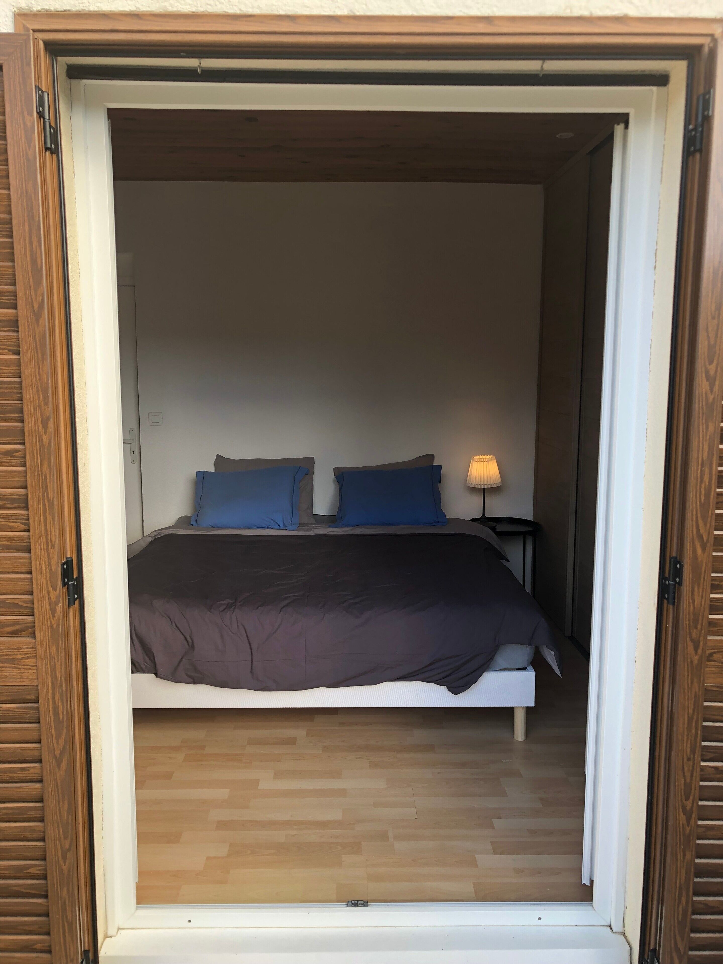 Un dormitorio con cama, almohadas, una mesita de noche y una lámpara.