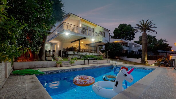 Ein Schwimmbecken mit Luftspielzeug, ein Haus mit Balkon und eine Palme.