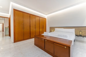 A modern bedroom with a large wooden wardrobe, a bed with white linens, and a headboard with horizontal slats.