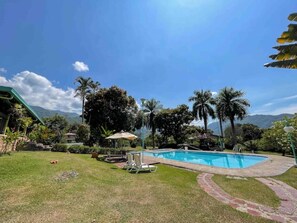 Une piscine entourée de palmiers, avec une chaîne de montagnes en arrière-plan.