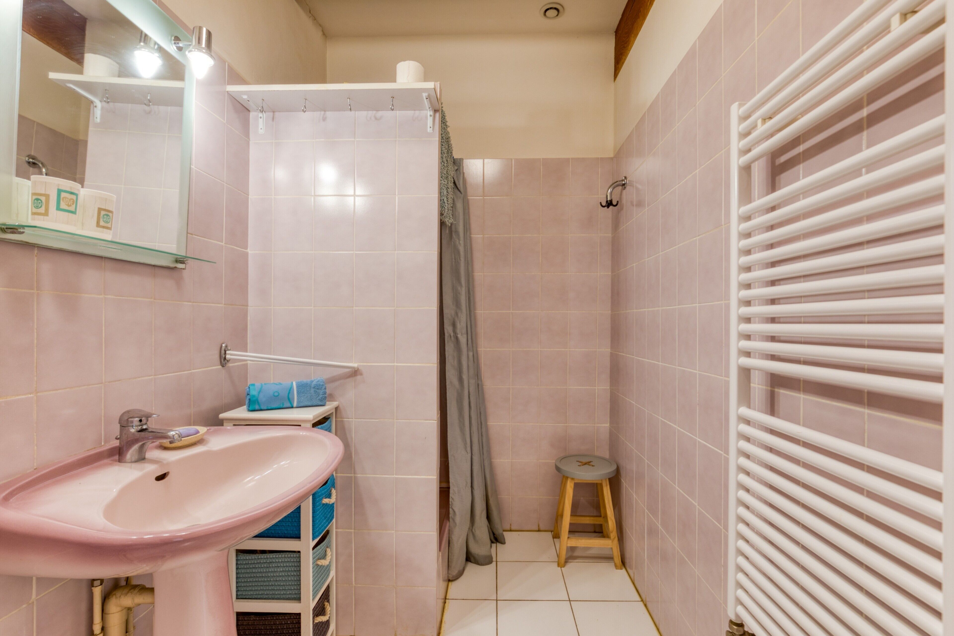 A bathroom with a pink sink, a mirror, a shower curtain, a towel rack, and a toilet.