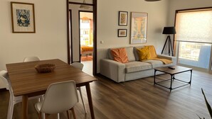 Een woonkamer met een bank, salontafel, eettafel, stoelen en kunstwerken aan de wanden.