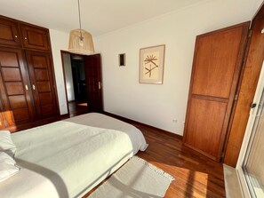 Une chambre à coucher avec un lit, une armoire en bois, un luminaire suspendu et deux tableaux encadrés accrochés au mur.