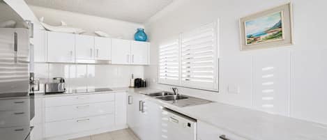 A modern kitchen with white cabinets, a stainless steel refrigerator, a Bosch dishwasher, and a window with white blinds.
