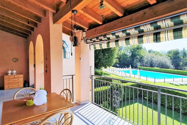 Un balcón con vista a una piscina, vigas de techo de madera y una mesa con sillas.