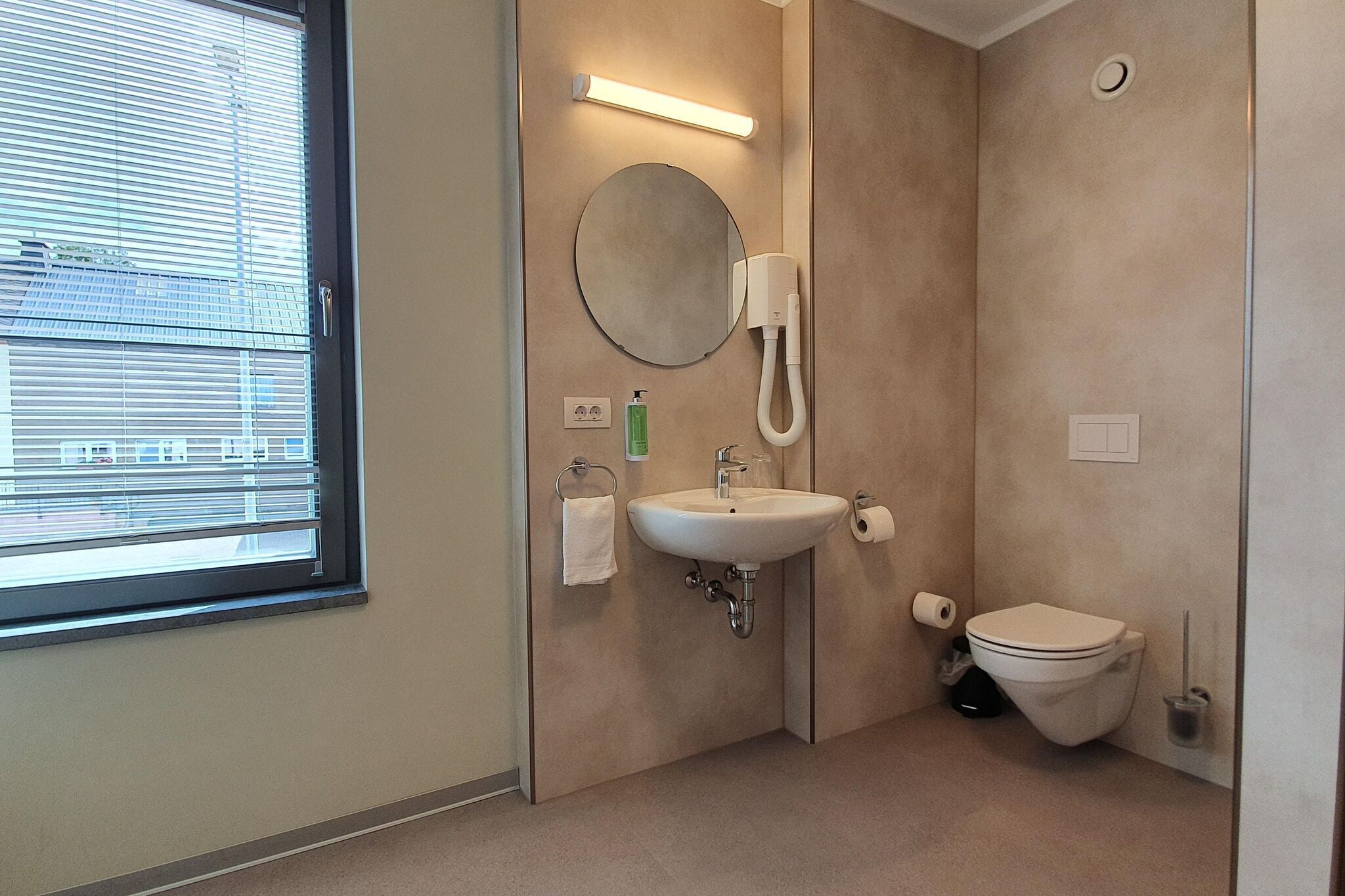 A modern bathroom with a sink, mirror, toilet, and window.