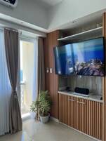 Una sala de estar moderna con un televisor de pantalla plana montado en una pared de paneles de madera, una planta en maceta y un ventanal corredero que da a un balcón.