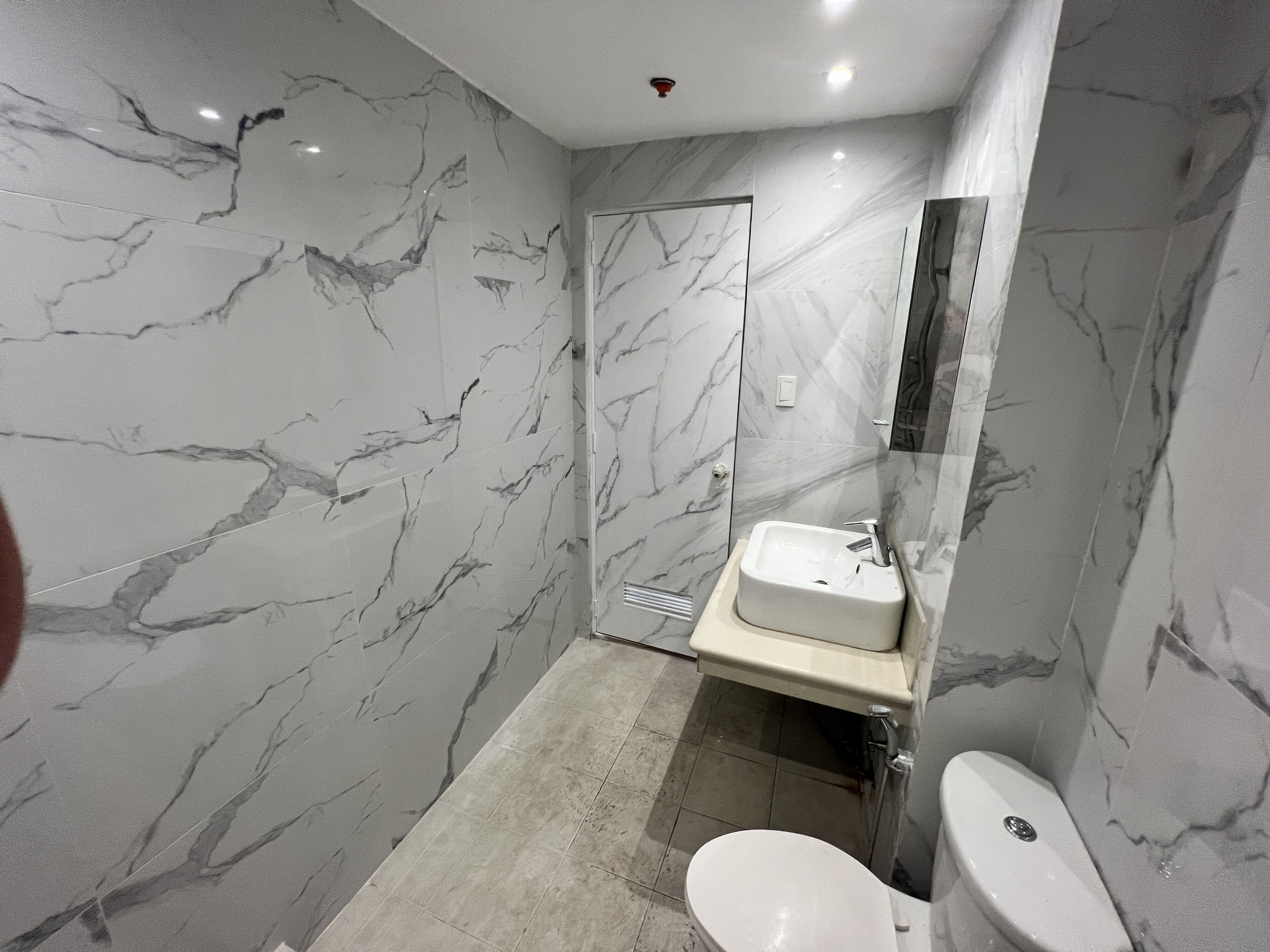 A modern bathroom with marble walls, a white sink, and a toilet.