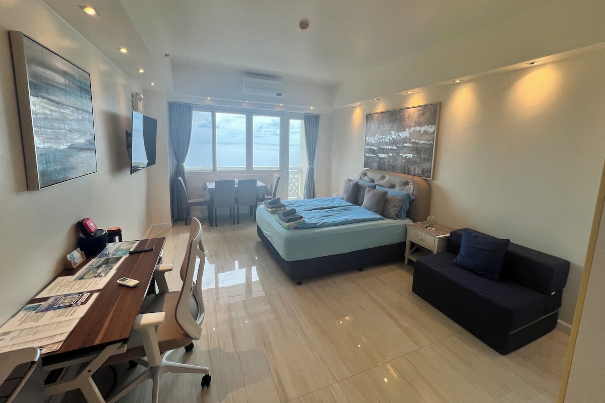 Ein Hotelzimmer mit Bett, Schreibtisch, Stuhl, einer Couch, einem Fernseher und einem Fenster mit Blick.