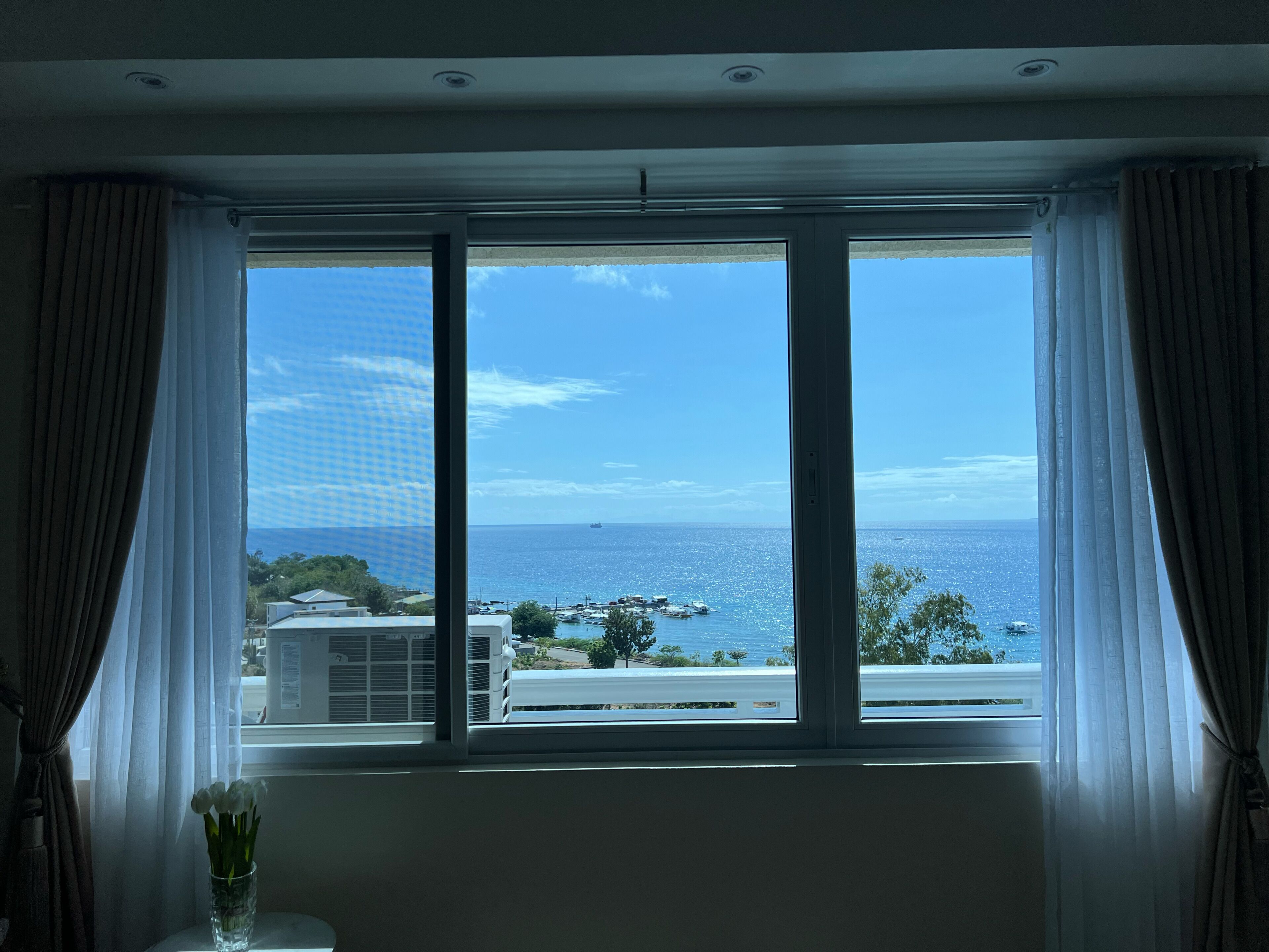 A room with a large window offering a view of the sea and buildings.