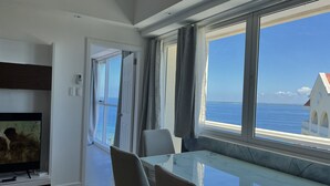 A modern living room with a glass table, a flat-screen TV, and a view of the sea. - La Mirada Residences spaces Sea-view Suites (Lapu-Lapu)