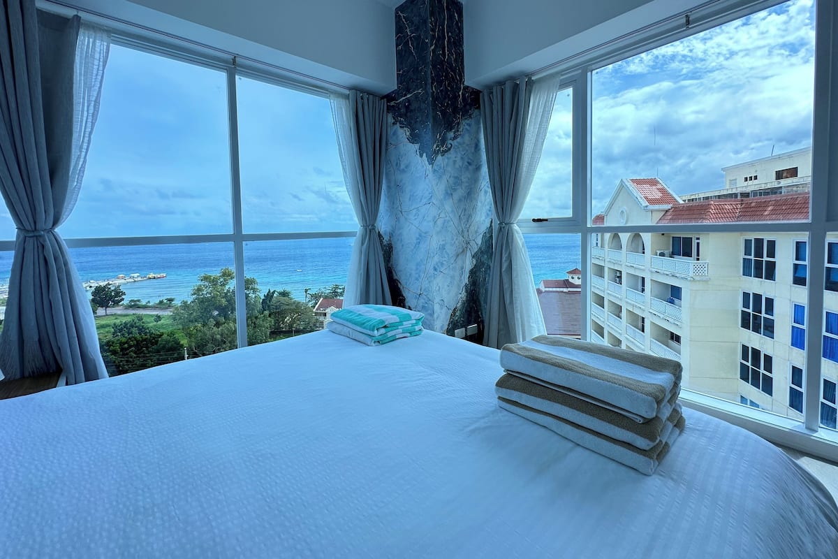 Ein Hotelzimmer mit einem großen Bett, Meerblick und einem Balkon mit Blick auf die Stadt.