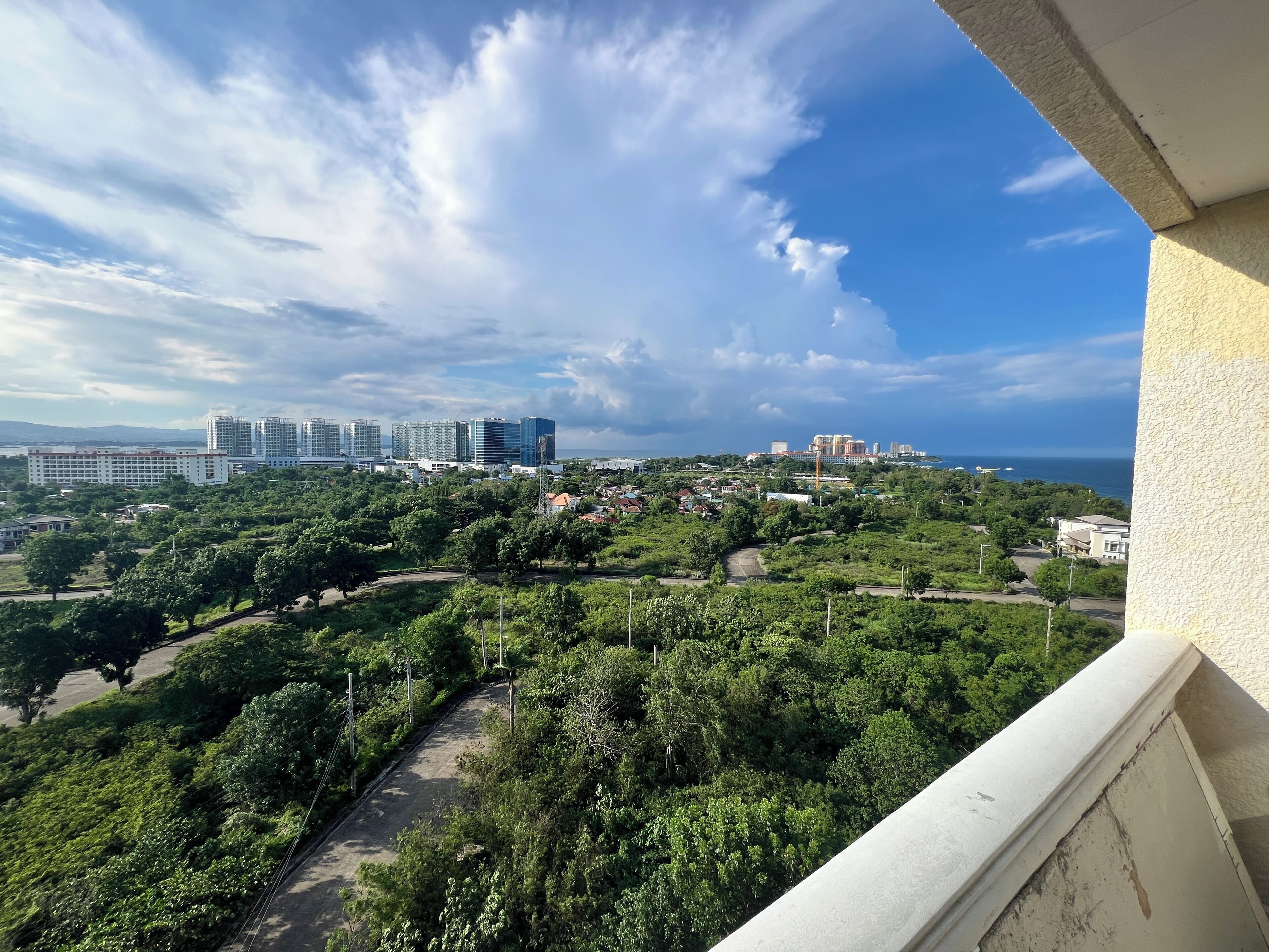 A balcony overlooking a cityscape with buildings, greenery, and a clear sky.