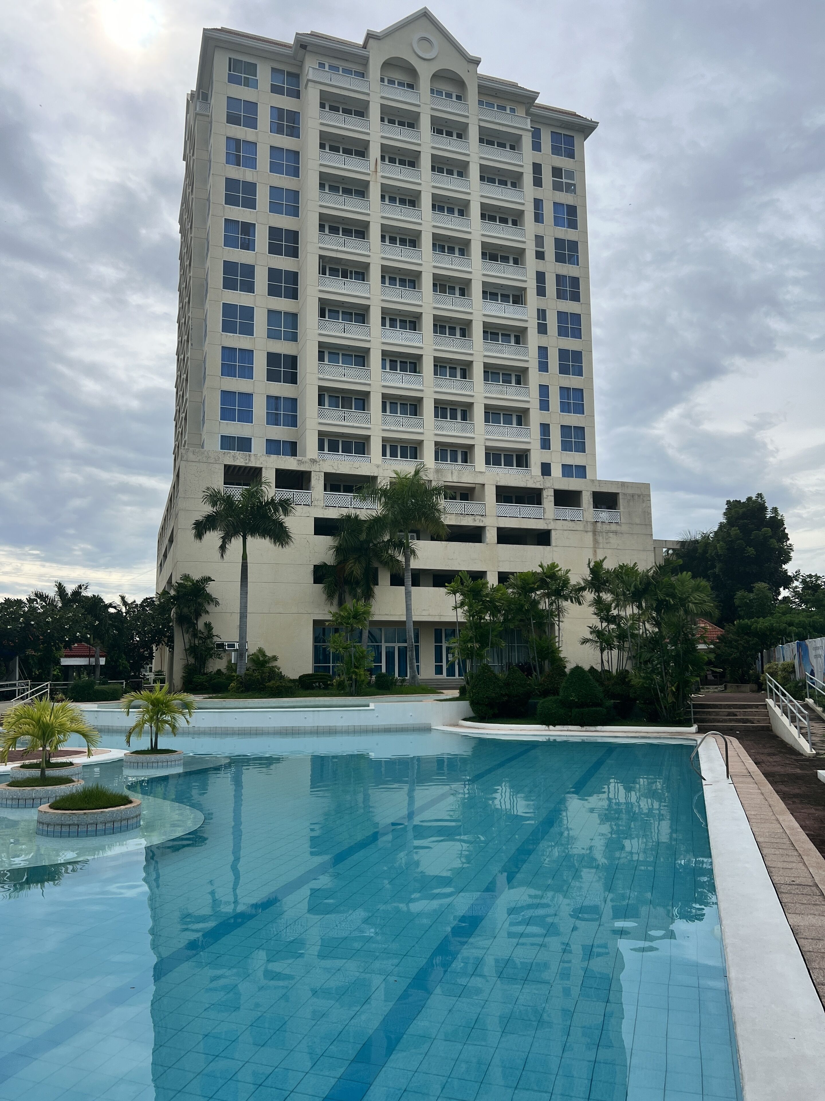 Ein Hotel mit großem Schwimmbad, mehreren Balkonen und üppiger Bepflanzung.