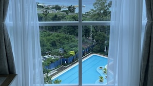 A room with a large window overlooking a swimming pool and a view of the sea. - La Mirada Residences spaces Sea-view Suites (Lapu-Lapu)