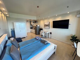 Un dormitorio moderno con cama, escritorio, televisor y kitchenette.