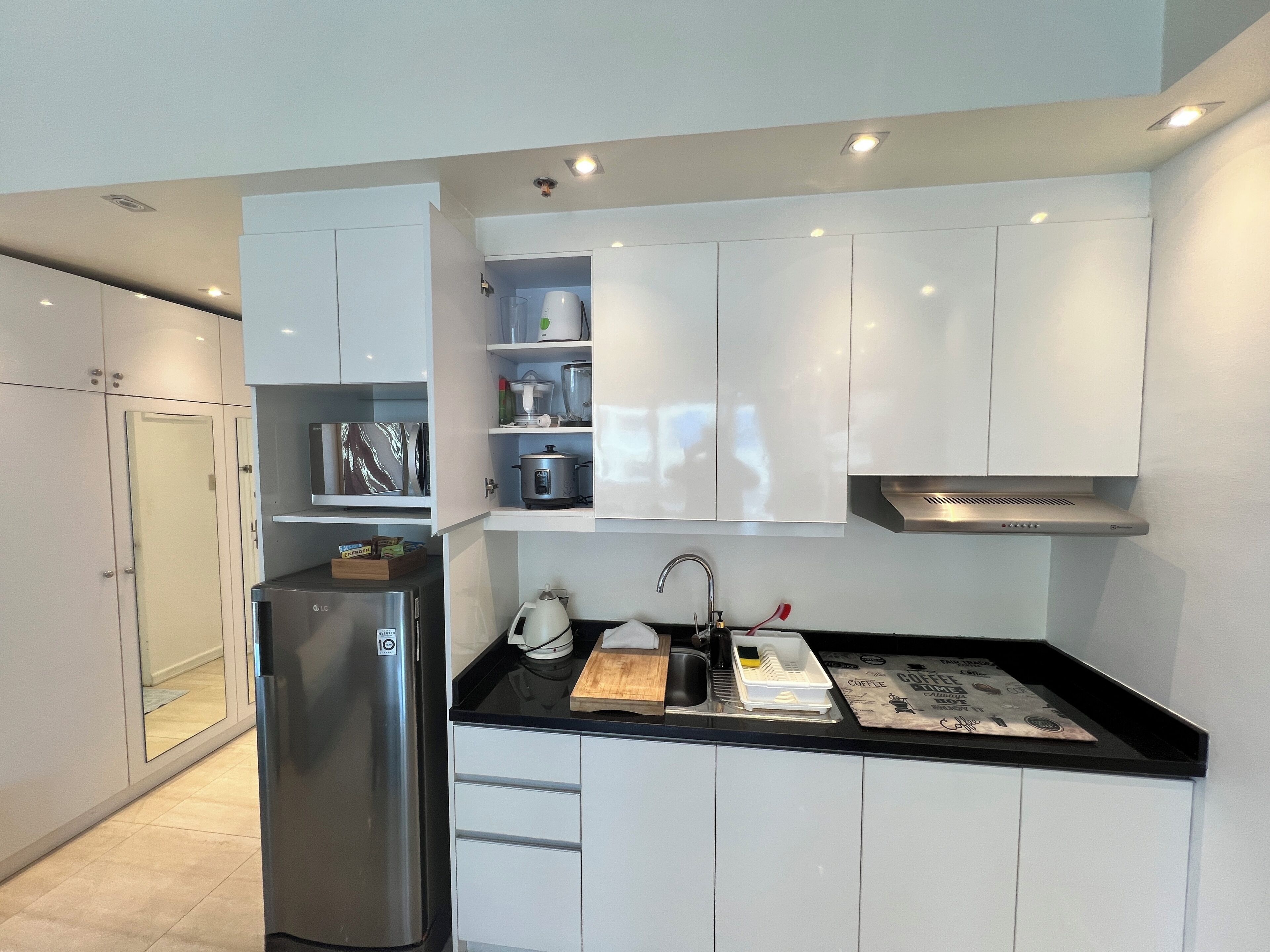 Cocina moderna con armarios blancos, un refrigerador de acero inoxidable, un lavamanos y una cafetera.