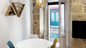 Un coin repas avec une table et des chaises blanches, un luminaire suspendu et un mur en pierre.