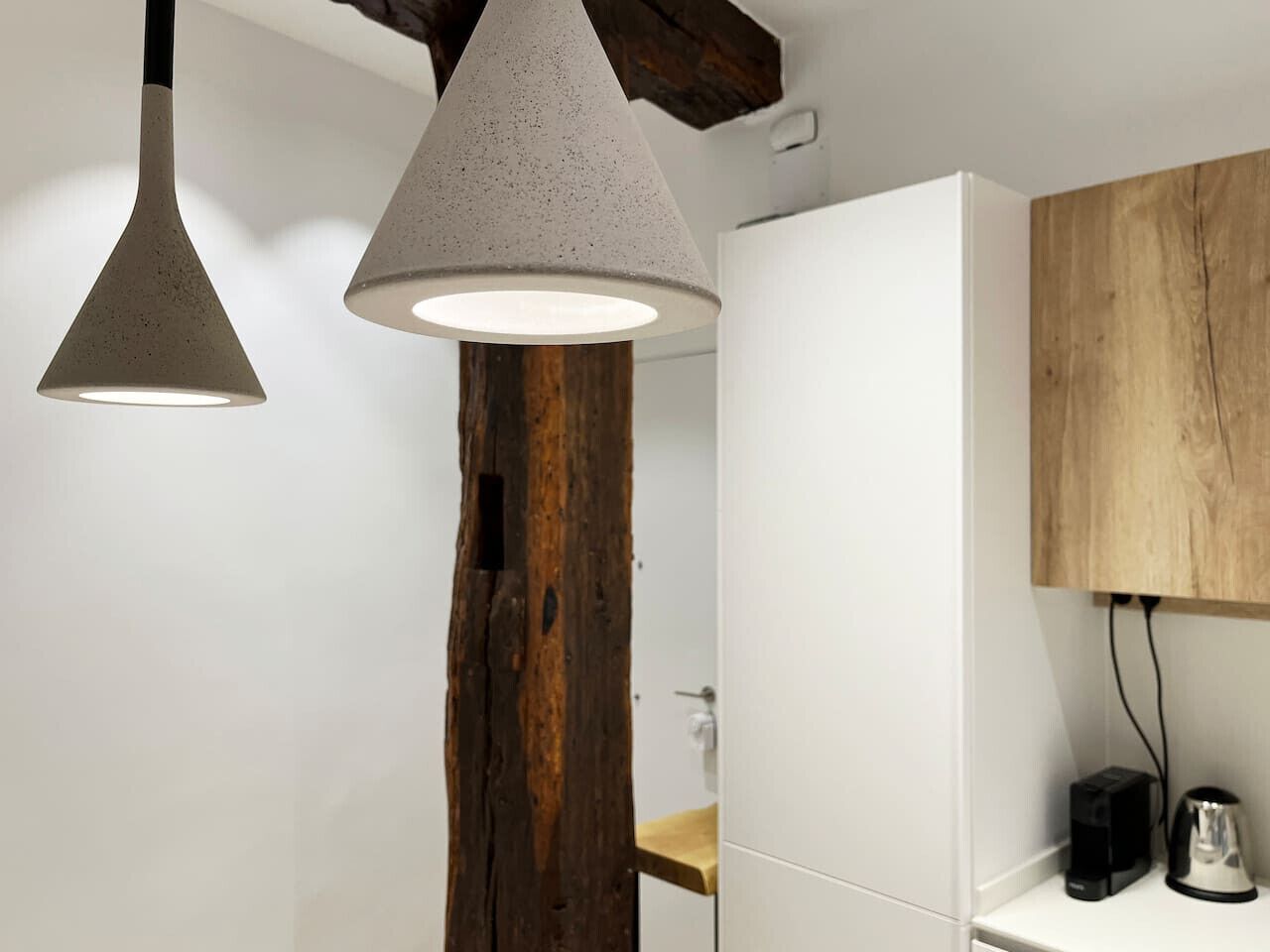 Una cocina moderna con una viga de madera, armarios blancos e iluminación colgante.