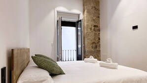 Une chambre avec un lit, un oreiller vert, des serviettes blanches et un mur en pierre.