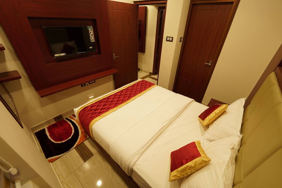 A hotel room with a bed, a TV mounted on the wall, and a door leading to another room.