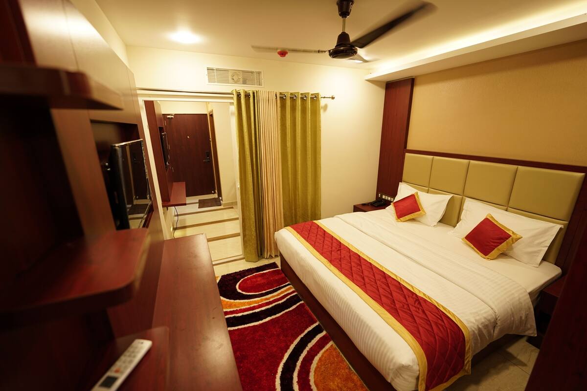 A hotel room with a bed, a desk, a chair, a ceiling fan, and a window with curtains.