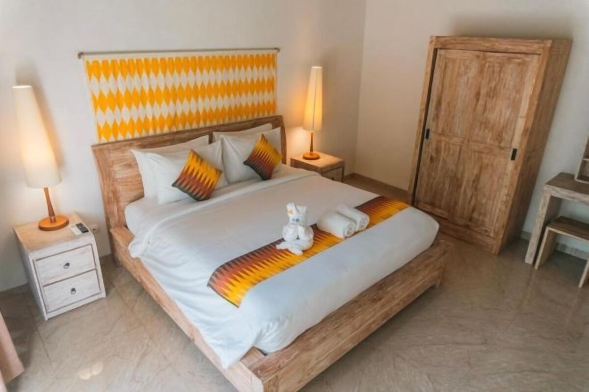 A neatly made bed with a patterned headboard, bedside lamps, and a wooden wardrobe.