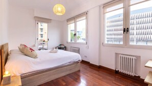 A bedroom with a large bed, a hanging light fixture, and large windows with blinds.