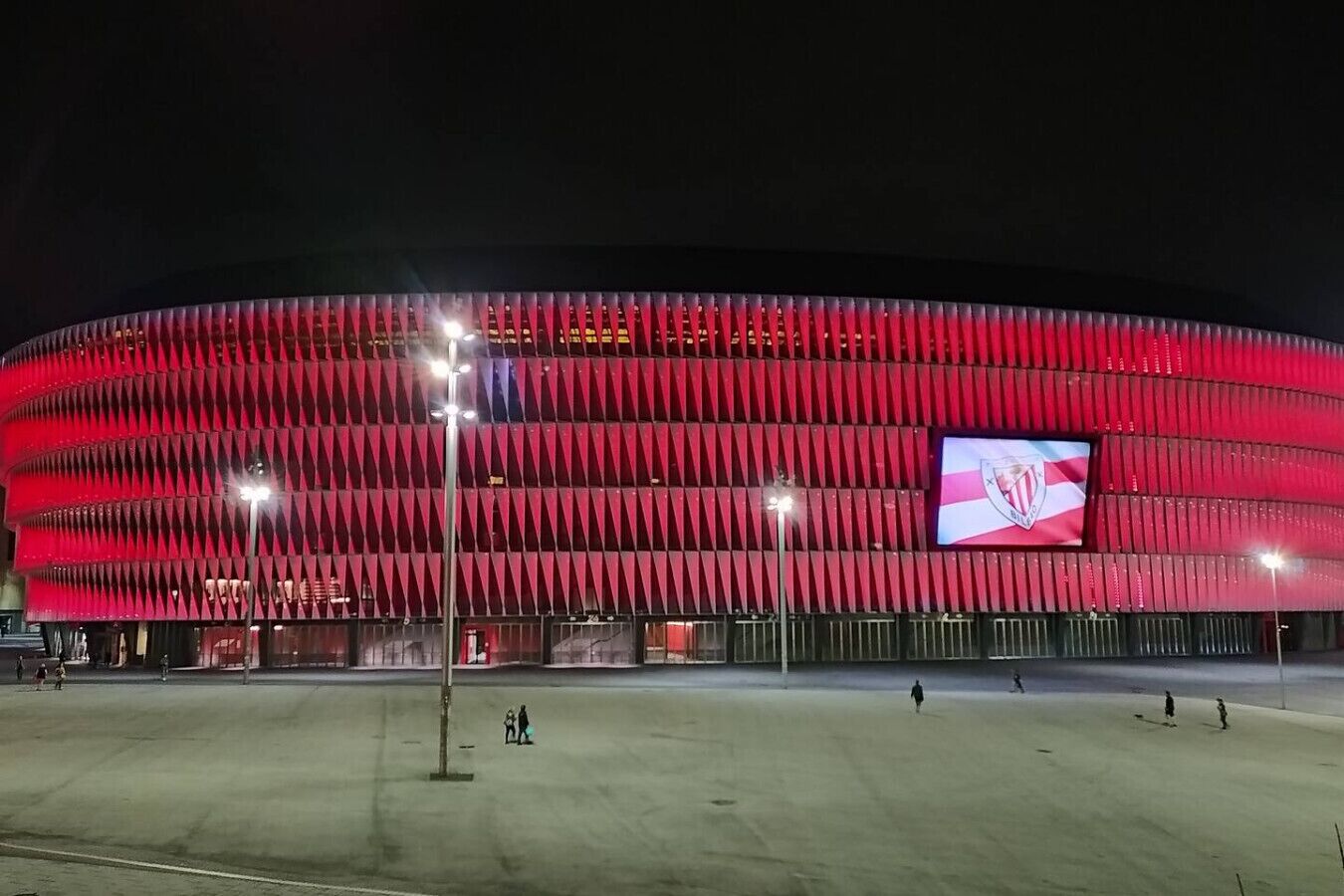 Un estadio con fachada roja y una gran pantalla digital que muestra un logotipo.