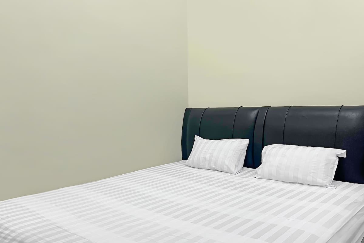 Una cama bien hecha con sábanas blancas y dos almohadas, un cabecero oscuro y una pared lisa.