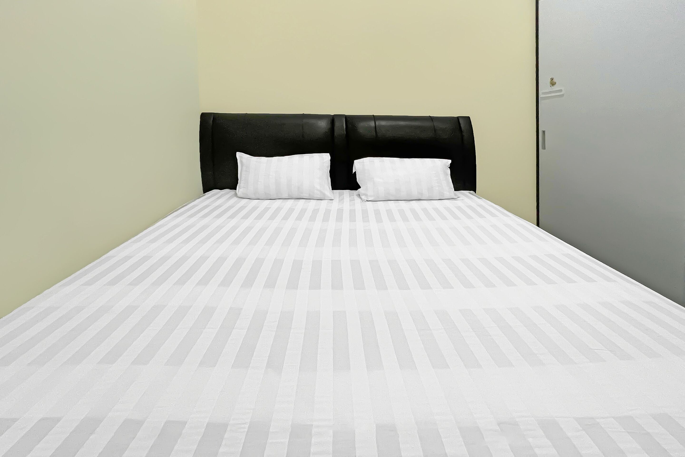 A bed with a striped bedspread and two pillows, a black headboard, and a light-colored wall.