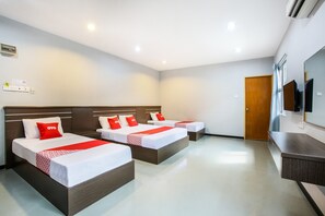 A hotel room with three beds, each with white bedding and red accents, a wooden headboard, a flat-screen TV, and a wooden door.