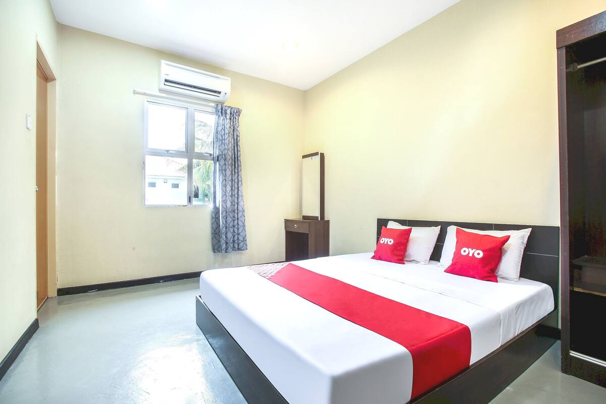 Une chambre d’hôtel avec un lit, une fenêtre avec des rideaux, un appareil de climatisation et une porte en bois.
