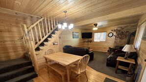 Et interiør i træ med trappe, spisebord med stole, sofa og fjernsyn.