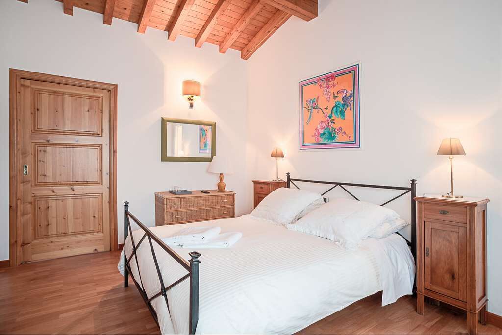 Quarto com cama de madeira, duas mesas de cabeceira, um criado-mudo, guarda-roupa e luminária na parede.