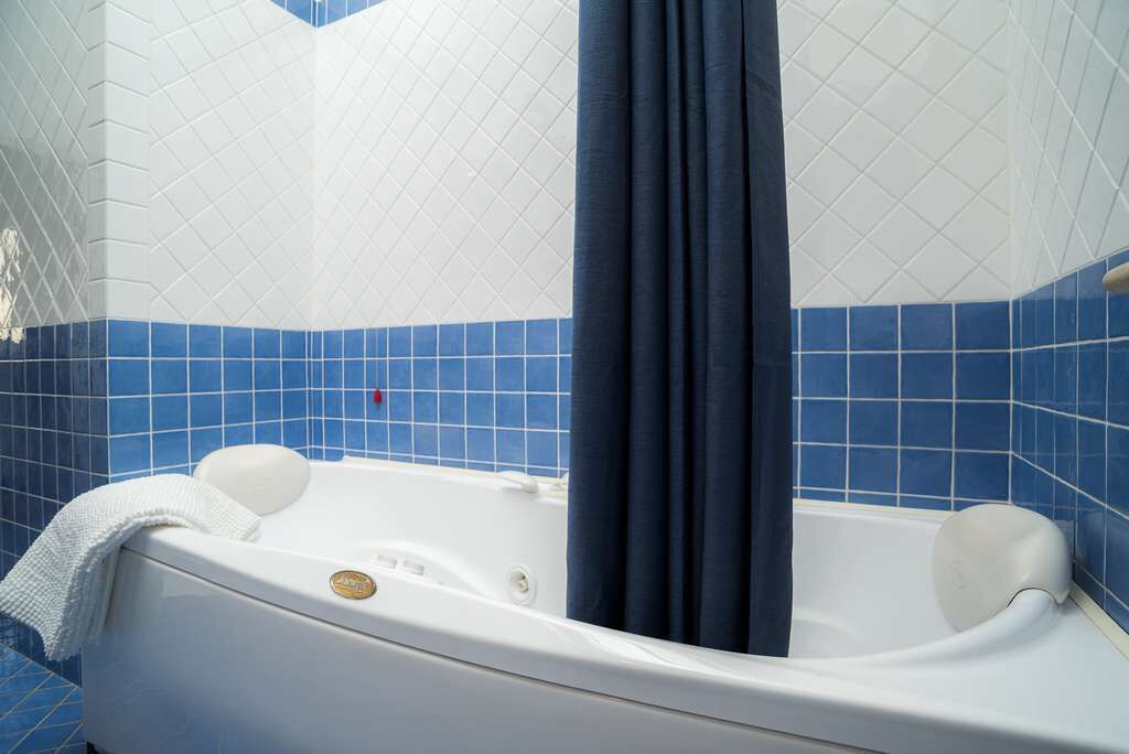 Una bañera con una cortina azul oscuro, azulejos blancos con un diseño de diamantes y una toalla blanca a un lado.