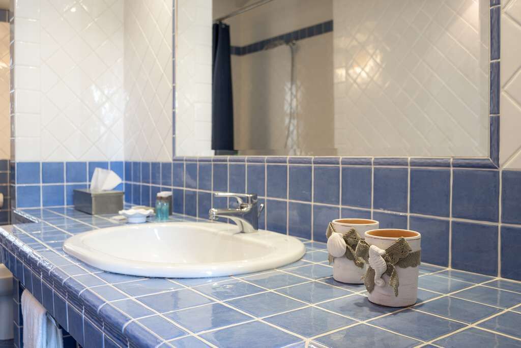 Un baño con un lavamanos blanco, azulejos azules y dos tazas decorativas sobre el mostrador.