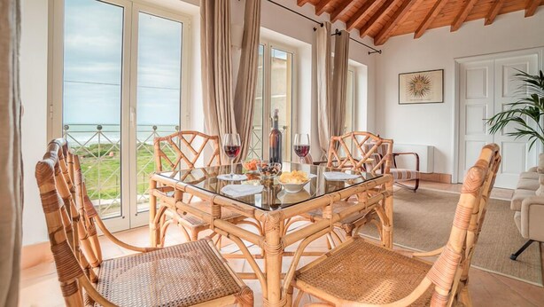 Un comedor con mesa de vidrio, sillas de mimbre y vistas al exterior.