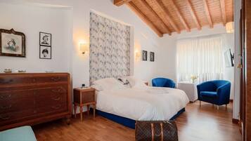 A bedroom with a wooden ceiling, a bed with a floral headboard, a dresser, a blue chair, and a small table with a lamp.