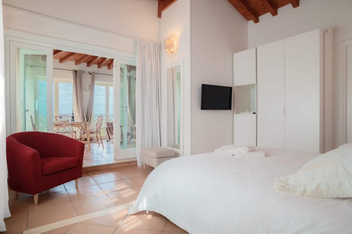 A bedroom with a large bed, a TV mounted on the wall, and a red chair.