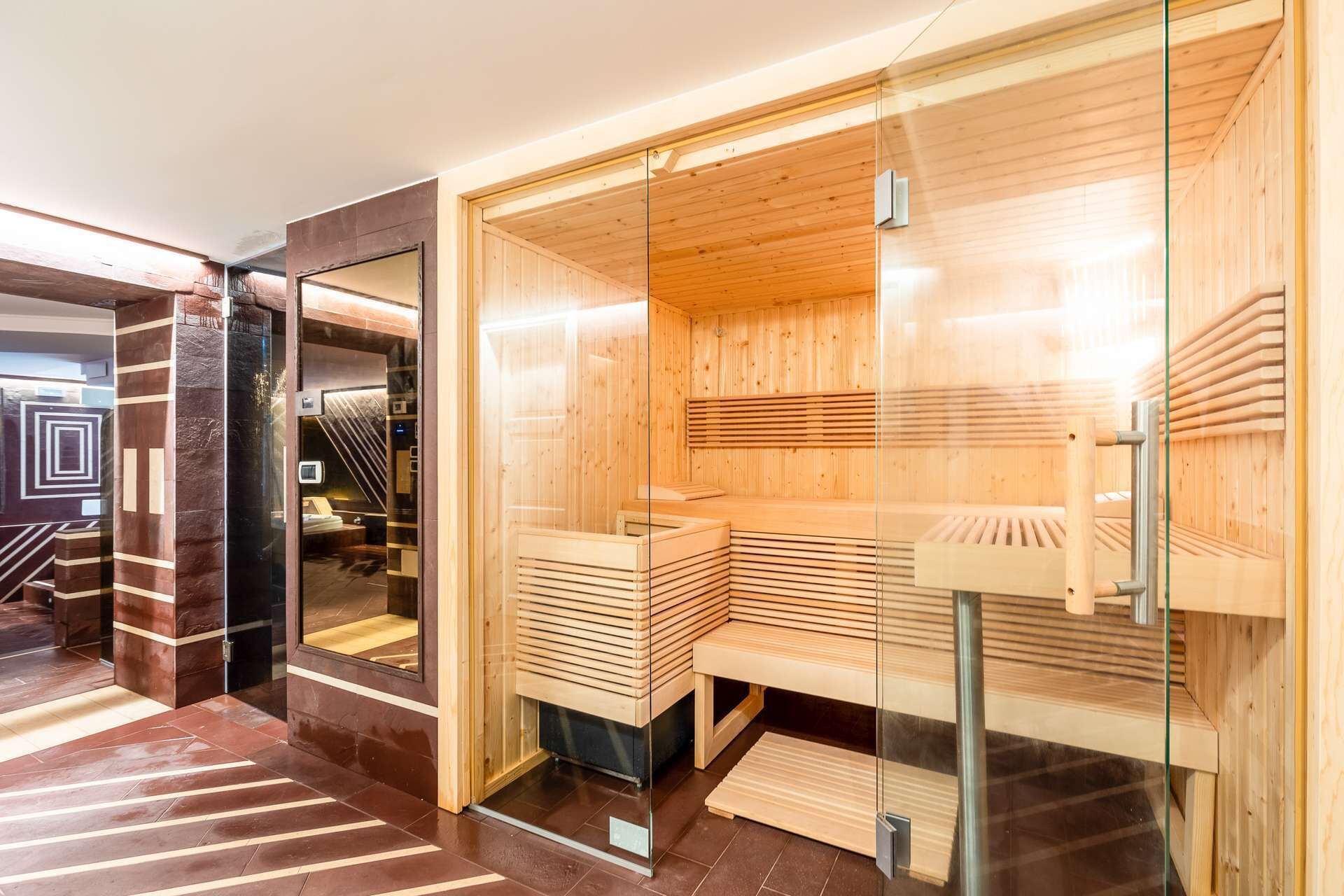 A sauna with wooden benches and glass doors, a tiled floor, and a modern interior design.