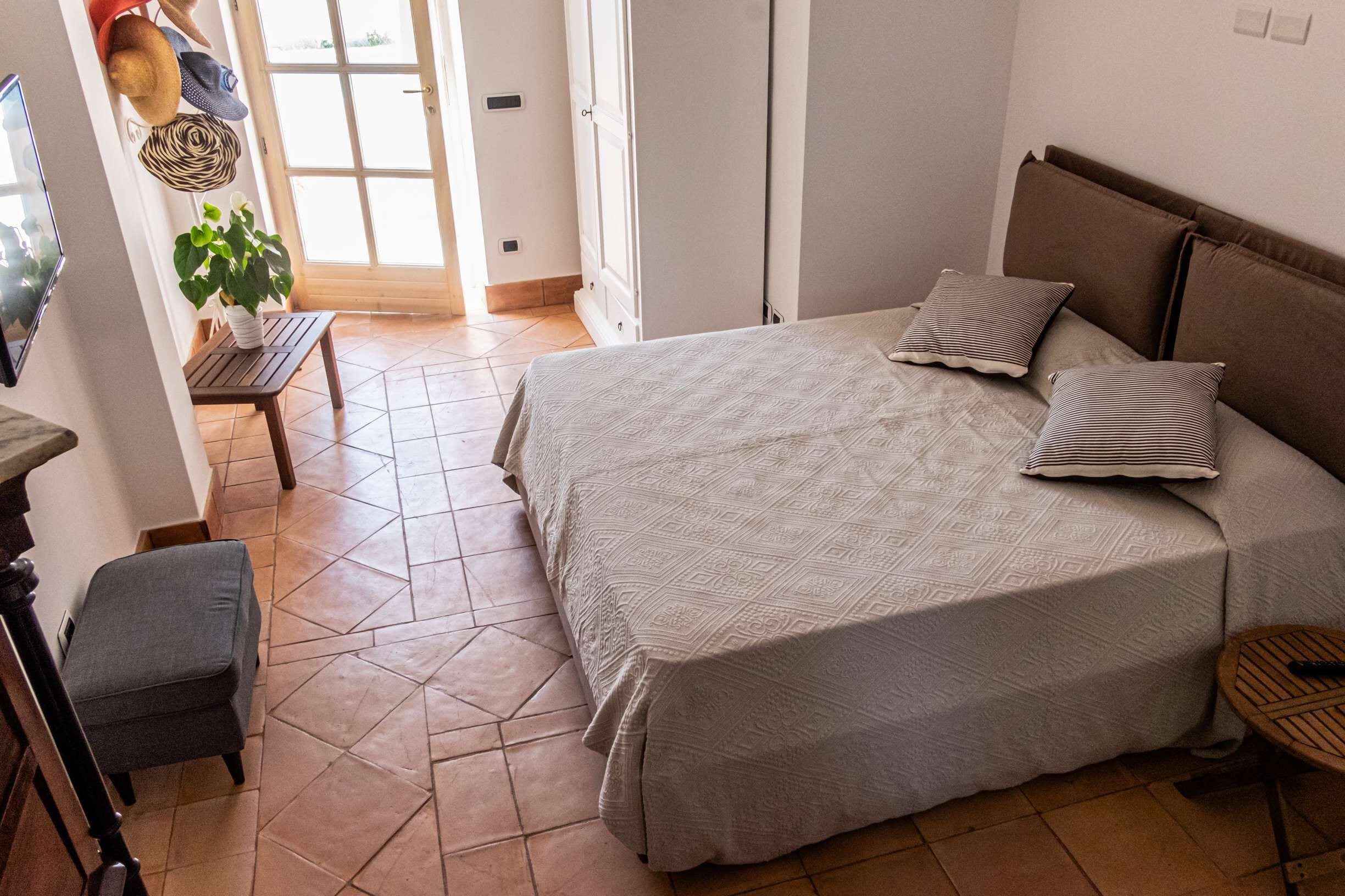 Un dormitorio con una cama grande, una mesita, una silla y una planta en maceta.