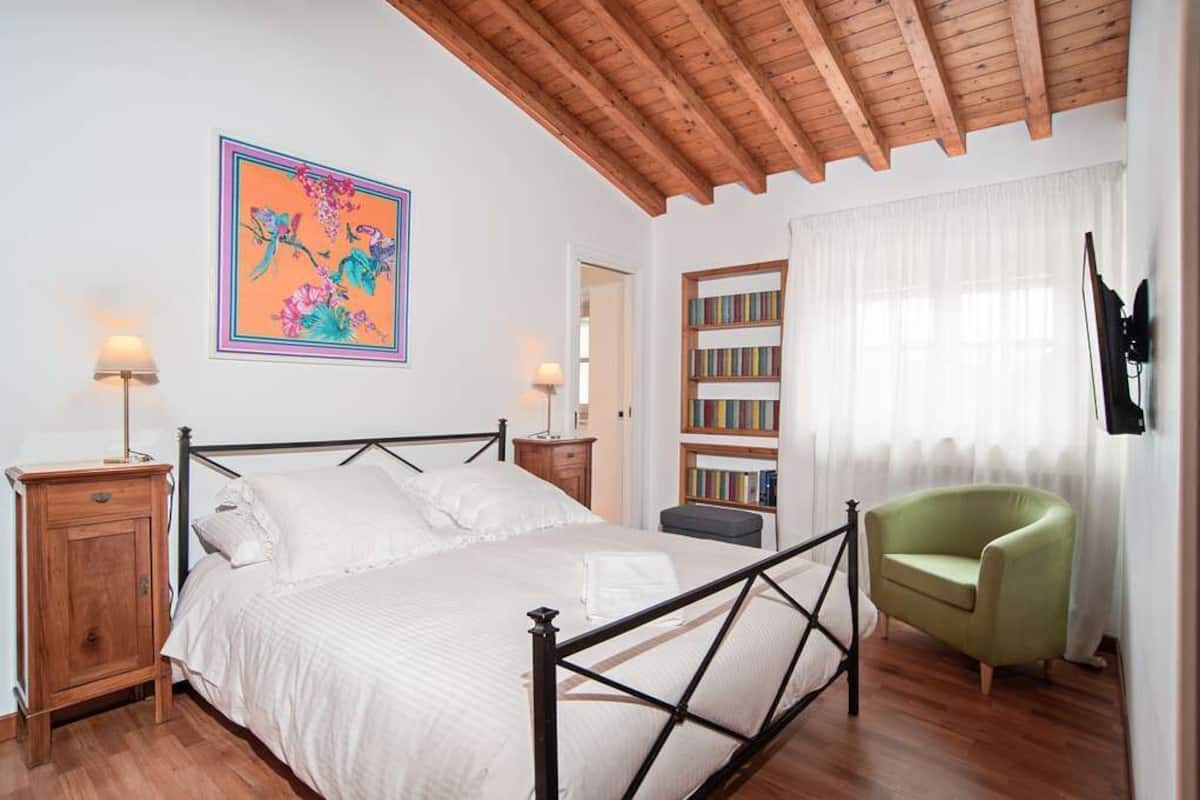 A bedroom with a bed, bedside tables, a bookshelf, a chair, and a painting on the wall.