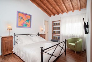 Ein Schlafzimmer mit Bett, Nachttischen, einem Bücherregal, einem Sessel und einem Bild an der Wand.